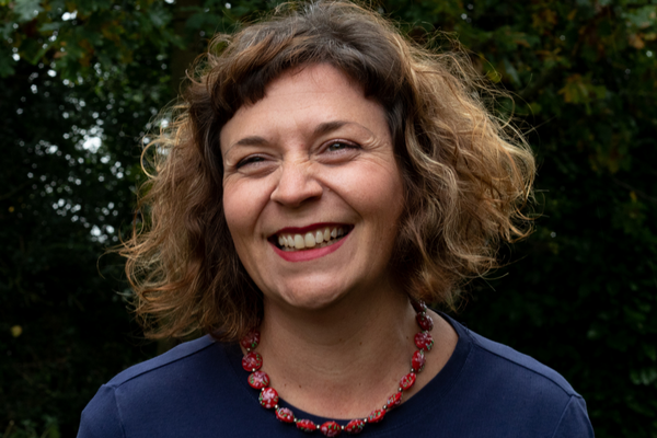 A smiley woman with brown curly hair and a red necklace on