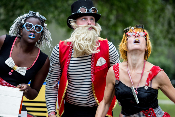 Group of three people wearing interesting costumes and glasses looking up at the sky