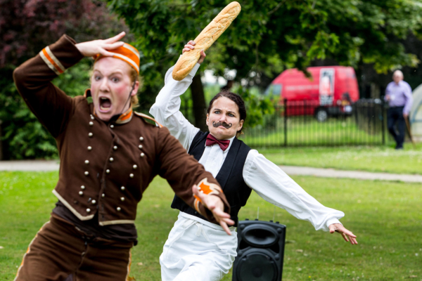 Two people dressed up in costume. They are running with the person at the back holding up a baguette.
