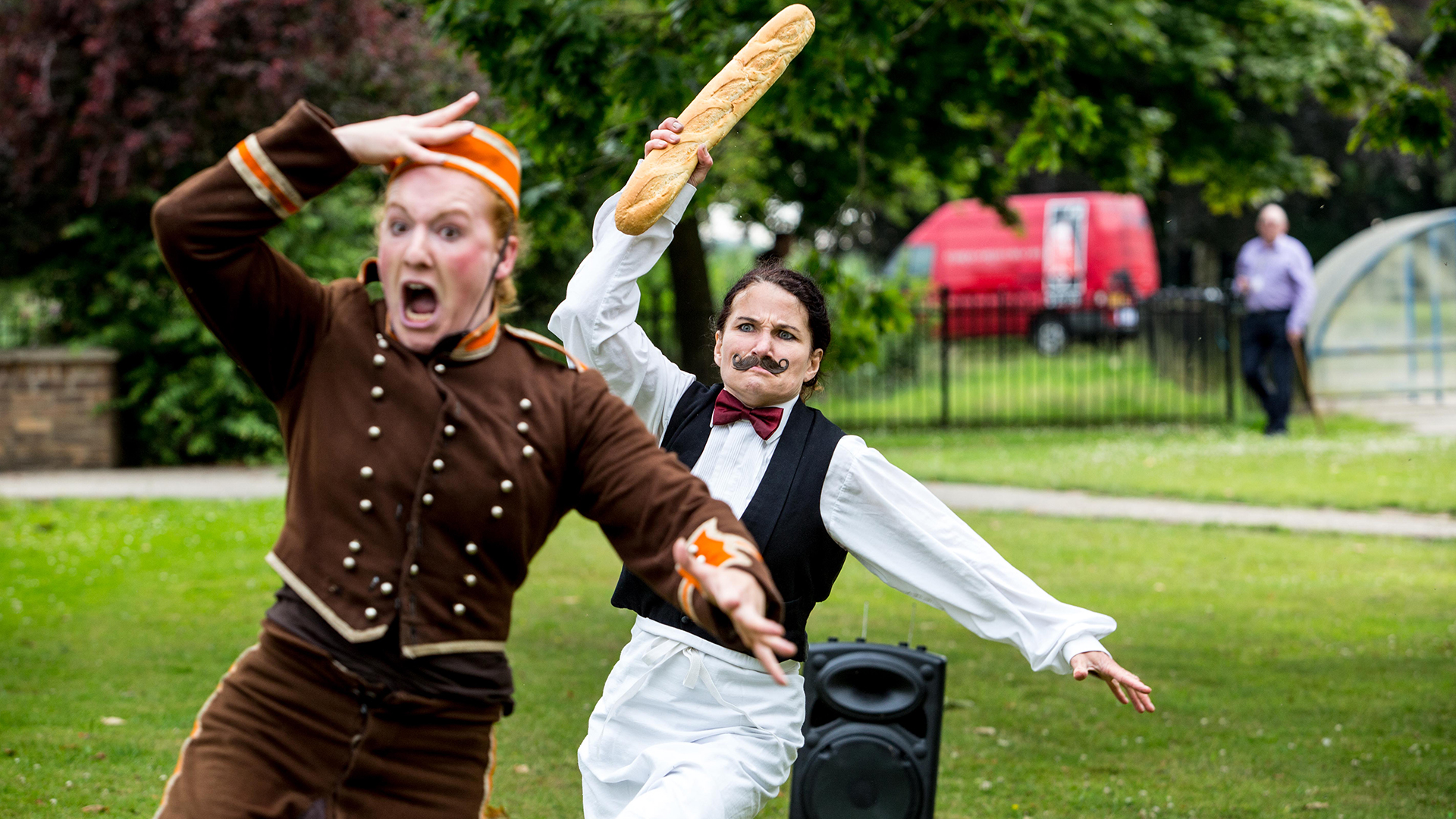 Two people dressed up in costume. They are running with the person at the back holding up a baguette.