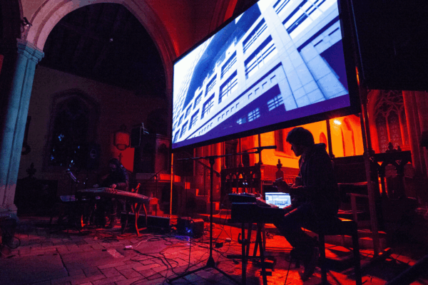 A large screen showing a film with a live performer