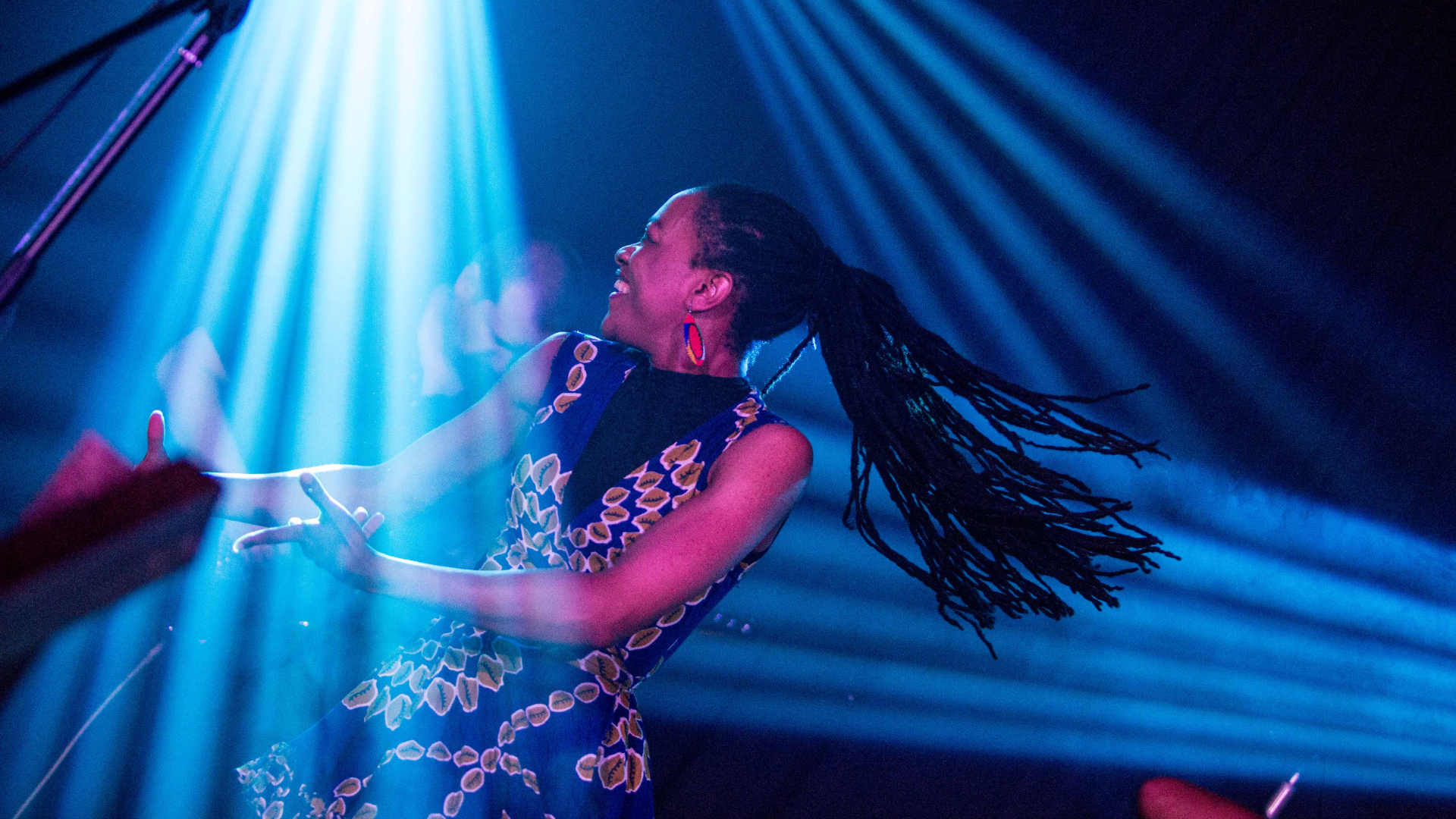 person on stage performing under blue strobe lights, their hair is long , dark and flicking to the right as they move