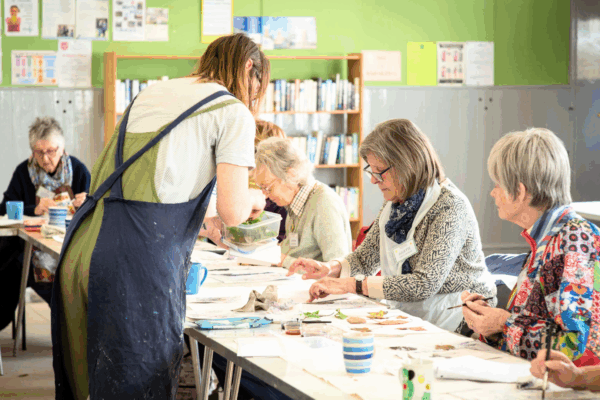 Image from the creative socials event. A group of older people sat on a long table taking part in crafts.