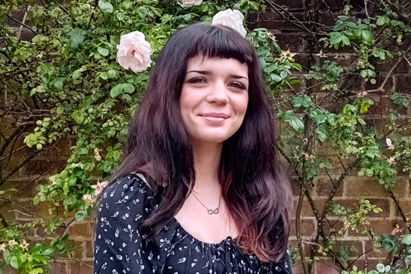 A girl with dark long hair stood in front of a rose bush